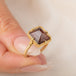 A gold ring featuring an Oregon Sunstone gemstone in a 18k gold bezel setting, held in hand.
