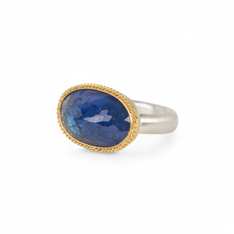 Handmade ring with blue tanzanite, gold bezel and sterling silver band on a white background