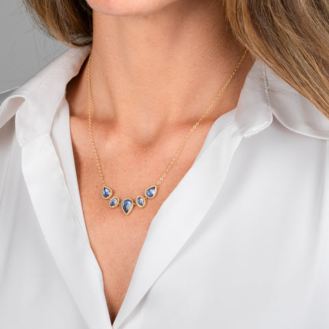 A gold necklace featuring five tanzanite gemstones in textured gold bezels, worn on a model's neck.