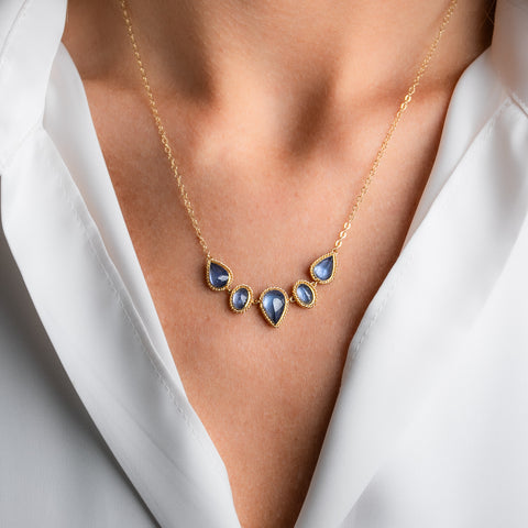 A gold necklace featuring five tanzanite gemstones in textured gold bezels, worn on a model's neck.