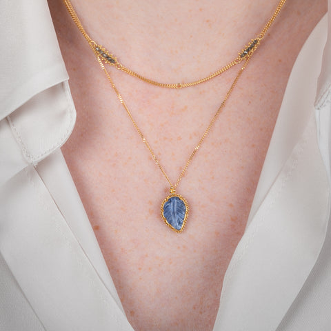 Gold necklace with a leaf-shaped tanzanite pendant on a person.