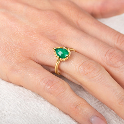 Gold ring with an Emerald gemstone on a person's finger against a neutral background