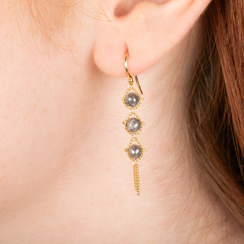 Gold earrings featuring trios of shimmering grey diamonds, shown worn in a person's ear.