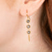 Gold earrings featuring trios of shimmering grey diamonds, shown worn in a person's ear.