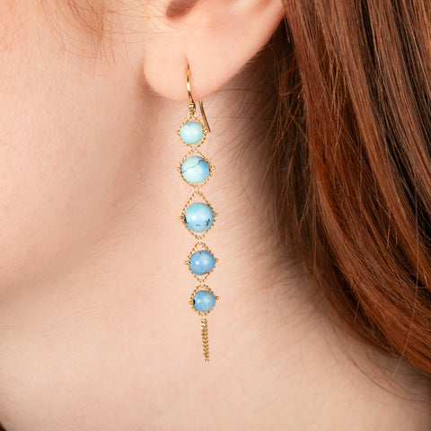 Gold earrings featuring golden hills turquoise stones worn in a person's ear.