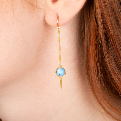 A gold earring featuring golden hills turquoise gemstones, shown worn in a person's ear.