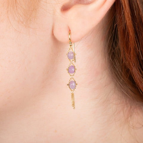 Gold earrings featuring a trio of holly blue chalcedony stones, worn on a person's ear.