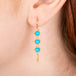 Gold earrings featuring trios of sleeping beauty turquoise gemstones, shown worn on a person's ear.