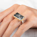 A rectangular ring featuring a tourmalated quartz crystal with visible needle-like inclusions, set in a gold bezel worn on a finger.