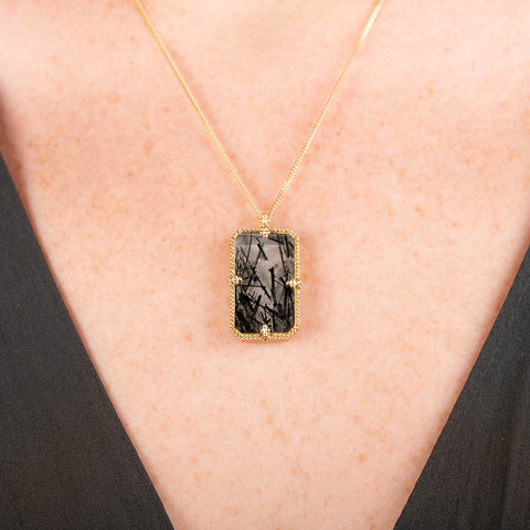 Handmade 18k yellow gold necklace with a tourmalated quartz pendant on a person