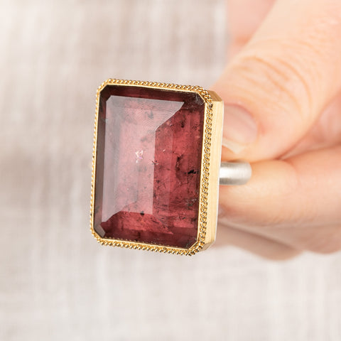 A close up of a person holding a handcrafted mixed metals ring with a tourmaline gemstone, 18k gold bezel and sterling silver band