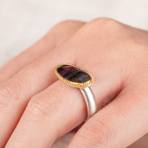 Hand wearing a watermelon tourmaline ring with gold bezel and silver band