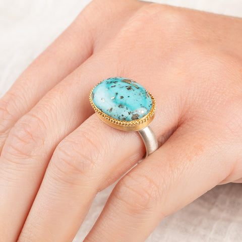 A close up of a person wearing a handmade fine jewelry turquoise ring with an 18k gold bezel and sterling silver band