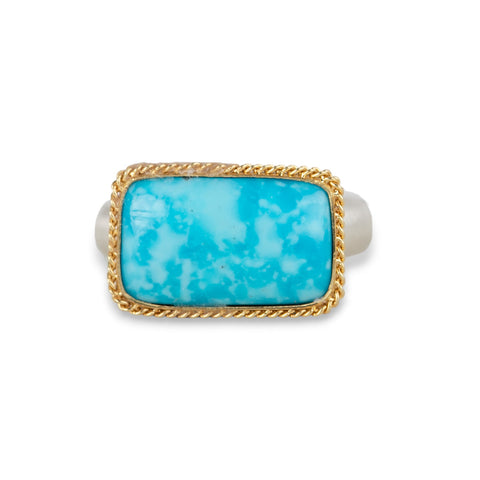 A gold ring featuring a rectangular turquoise stone set in a gold bezel with a sterling silver band against a plain white background.