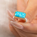 A gold ring featuring a rectangular turquoise stone set in a gold bezel with a sterling silver band held in hand