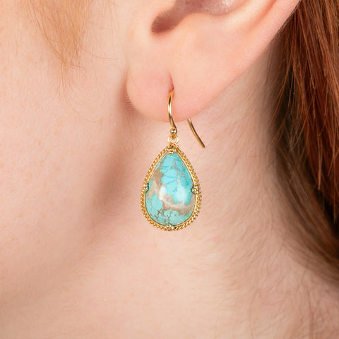 Gold earrings featuring turquoise gemstones, shown worn in a person's ear.
