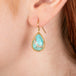 Gold earrings featuring turquoise gemstones, shown worn in a person's ear.