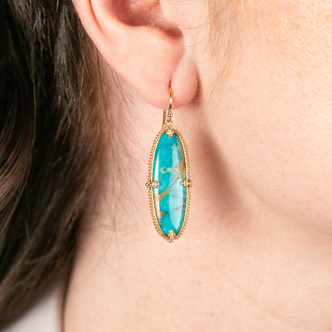 Turquoise earring with gold bezel worn by a person
