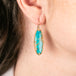 Turquoise earring with gold bezel worn by a person