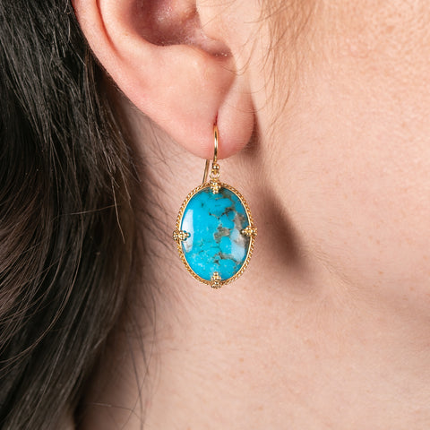 Turquoise earring with gold setting worn by a person