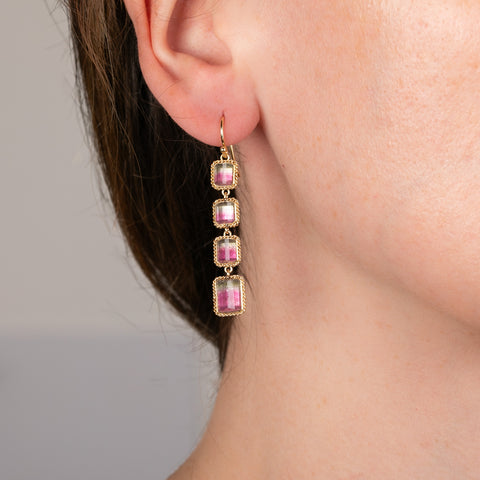 Close-up of a person wearing watermelon tourmaline gemstone earrings with gold setting.