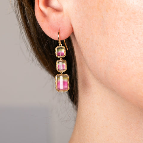 Close-up of a person wearing a handamde gold earring with watermelon tourmaline gemstones on a neutral background.