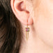 A person wears gold earrings with watermelon tourmaline gemstones and gold chain tassels