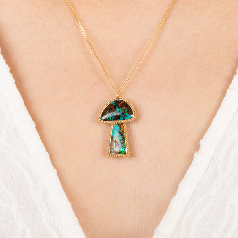 Gold mushroom necklace with a colorful boulder opal pendant on a person wearing a white top.