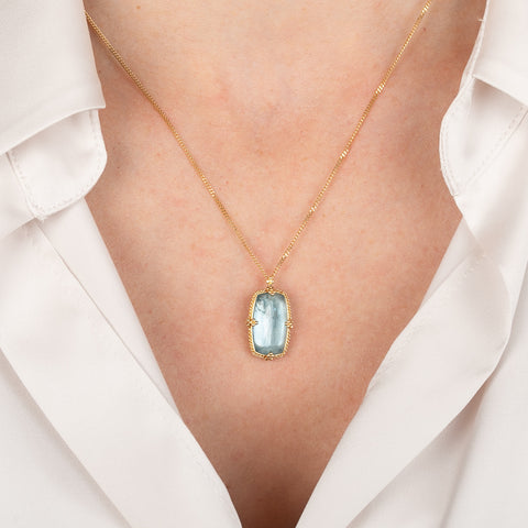 Gold necklace with an aquamarine gemstone pendant on a person