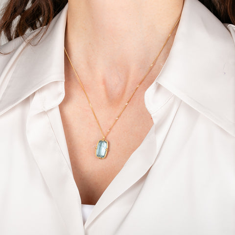 Gold necklace with an aquamarine gemstone pendant on a person