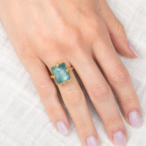 Gold ring with a rectangular aquamarine gemstone on a hand