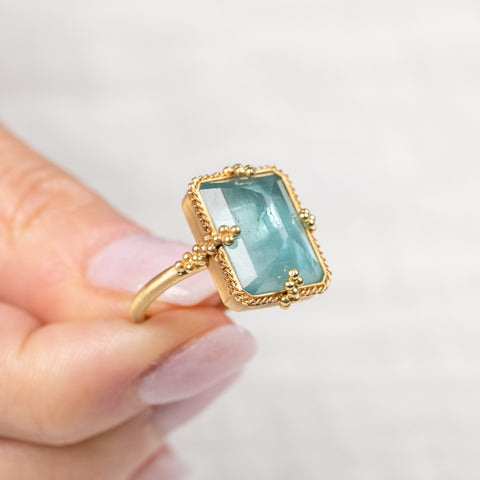 Gold ring with a blue aquamarine gemstone held by a hand on a light background
