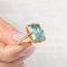 Gold ring with a blue aquamarine gemstone held by a hand on a light background