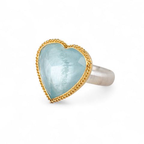 Heart-shaped ring with aquamarine stone, gold bezel and silver band on a white background