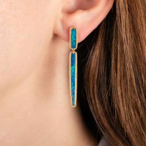 A pair of gold post earrings with Australian opal doublets, worn in a model's ear.
