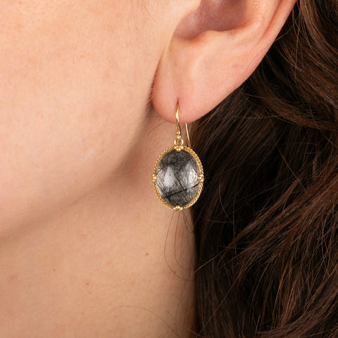 Gold earrings featuring toumalated quartz worn by a person