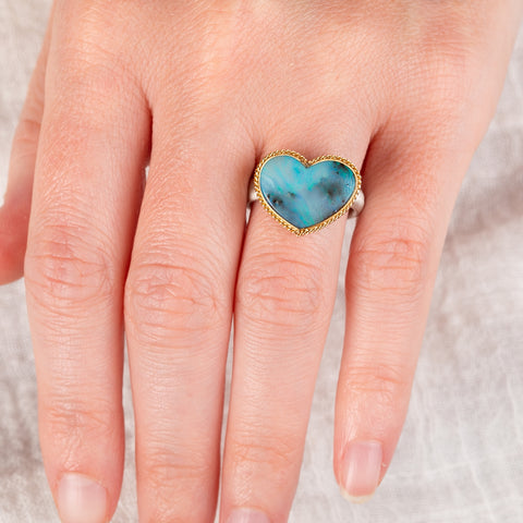 Hand wearing a boulder opal heart ring with a gold bezel and silver band