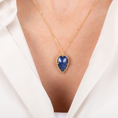 Gold necklace with a blue teardrop-shaped tanzanite gemstone pendant on a person