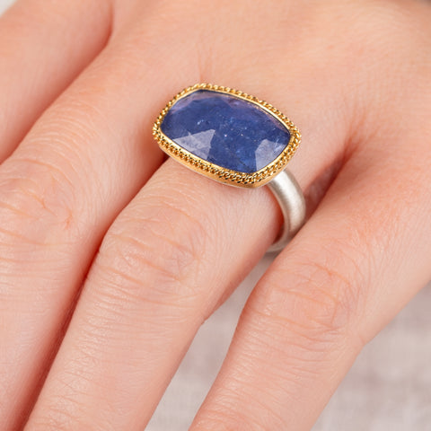 Close up of hand wearing a tanzanite gemstone ring with gold bezel and silver band