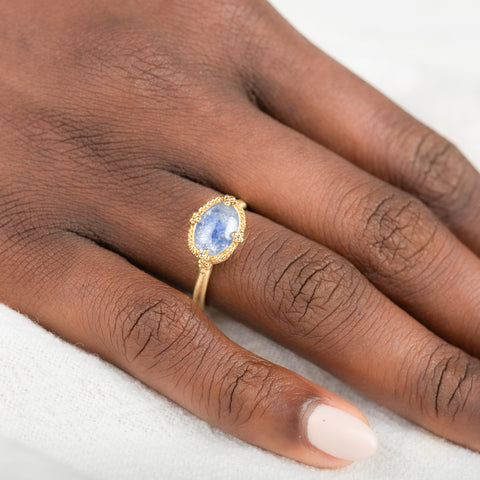 Gold ring with a blue dumortierite stone on a person's finger