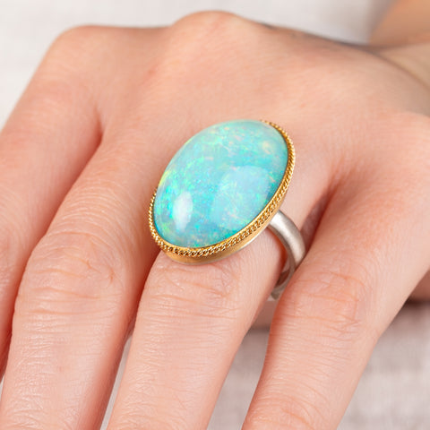 Hand wearing an Ethiopian opal ring with gold bezel and sterling silver band