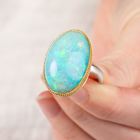 Hand holding an Ethiopian opal ring with gold bezel and sterling silver band