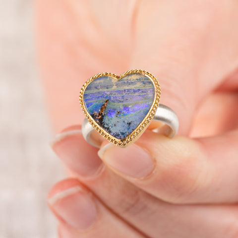 Hand holding a boulder opal heart ring in an 18k gold bezel with sterling silver band