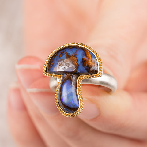 Hand holding a boulder opal mushroom ring in gold and silver