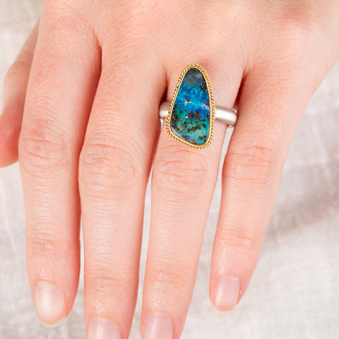 A hand wears a boulder opal ring with an 18k gold bezel and sterling silver band