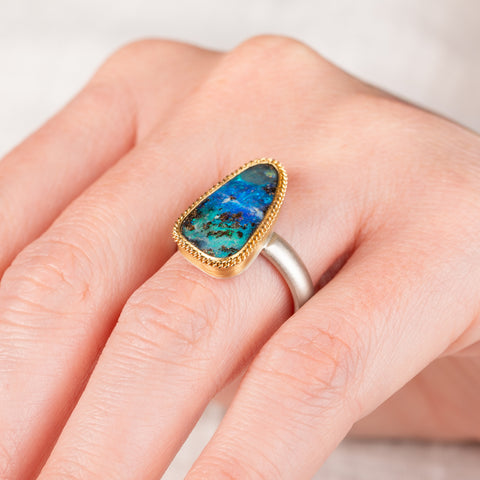 A hand wears a boulder opal ring with an 18k gold bezel and sterling silver band