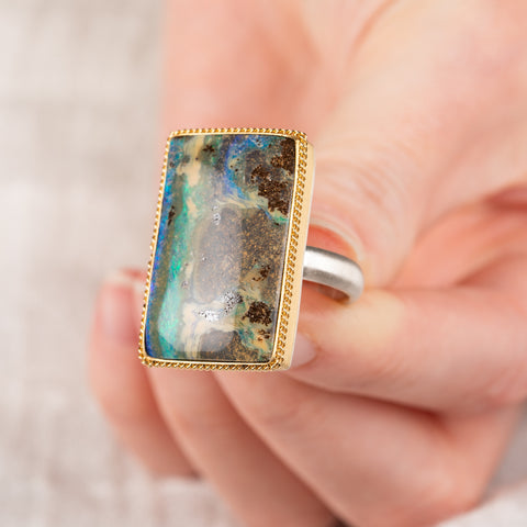 Hand holding a boulder opal ring in 18k gold bezel and sterling silver band