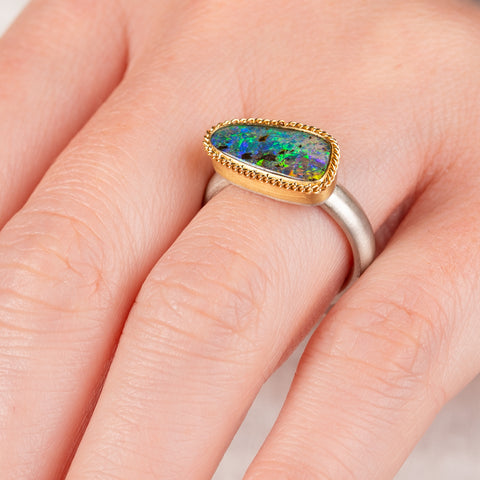Close up of hand wearing a boulder opal ring with gold bezel and sterling silver band