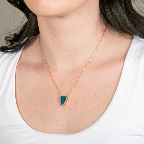 Gold necklace with a triangular boulder opal pendant on a person