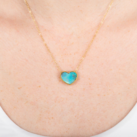 Necklace with a heart-shaped boulder opal stone pendant on a gold chain against a person